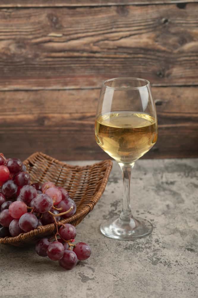 wicker-basket-of-red-grapes-with-glass-of-white-wine-on-marble-table